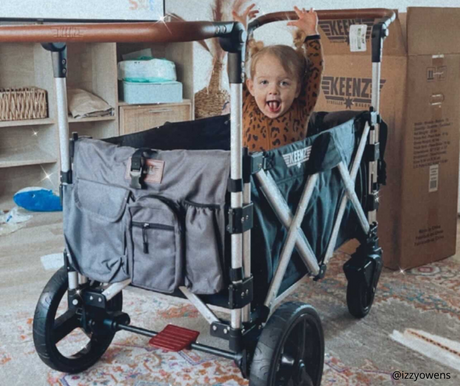 excited baby sticking tongue out and raising hands in cheer while sitting in black Keenz stroller wagon