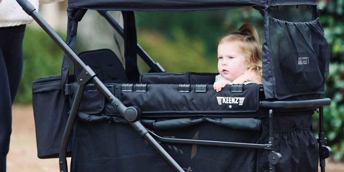 Toddler seated under the canopy of a black Keenz VIVA stroller wagon