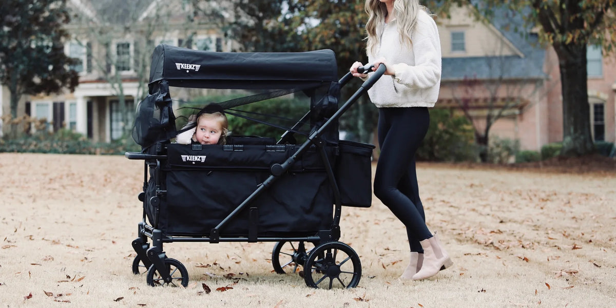 Mother pushing a toddler in a black Keenz VIVA stroller wagon in front of a house