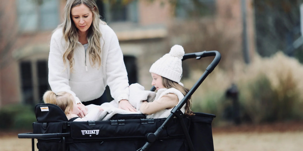 Mother settling two children into the seats of a black Keenz stroller wagon