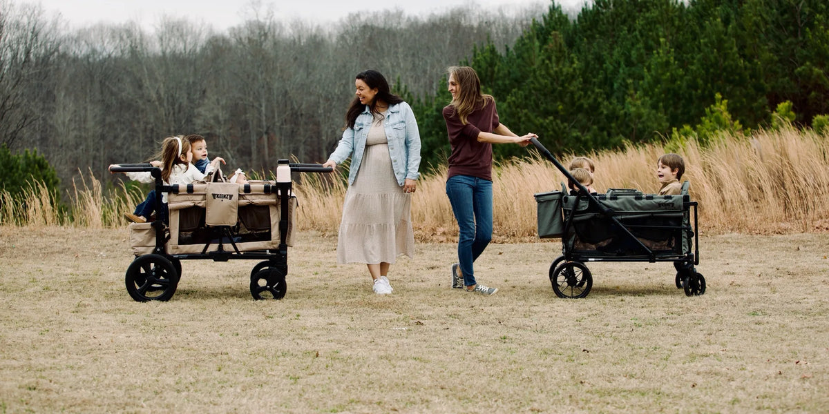 Parents pushing and pulling two Keenz stroller wagons with children through a field