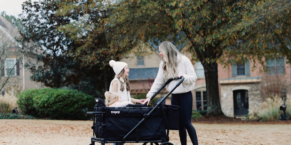 Mother walking beside a black Keenz stroller wagon as her children ride in the yard
