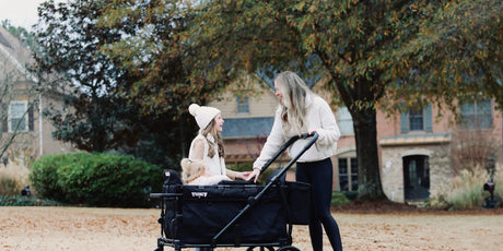 Mother walking beside a black Keenz stroller wagon as her children ride in the yard