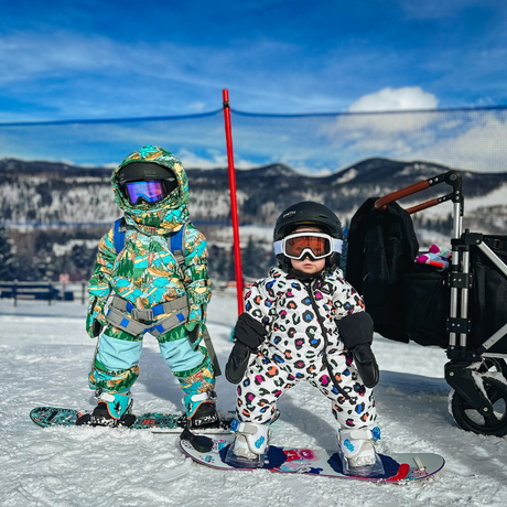 two children in full snowboarding gear pose in front of black Keenz stroller wagon