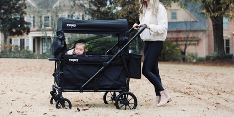 A parent pushing a compact stroller wagon with children along a paved park path