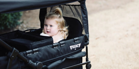 Caregiver guiding a child in a stroller wagon along a park path