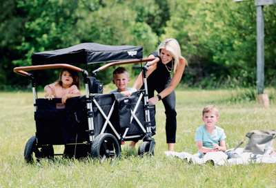two kids enjoy mom pushing them in black Keenz stroller wagon during family picnic