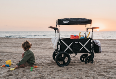 black Keenz stroller wagon at beach with toddler playing in sand during sunset over the ocean