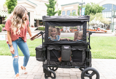 four kids in black Keenz stroller wagon with mom pushing them in the cityscape